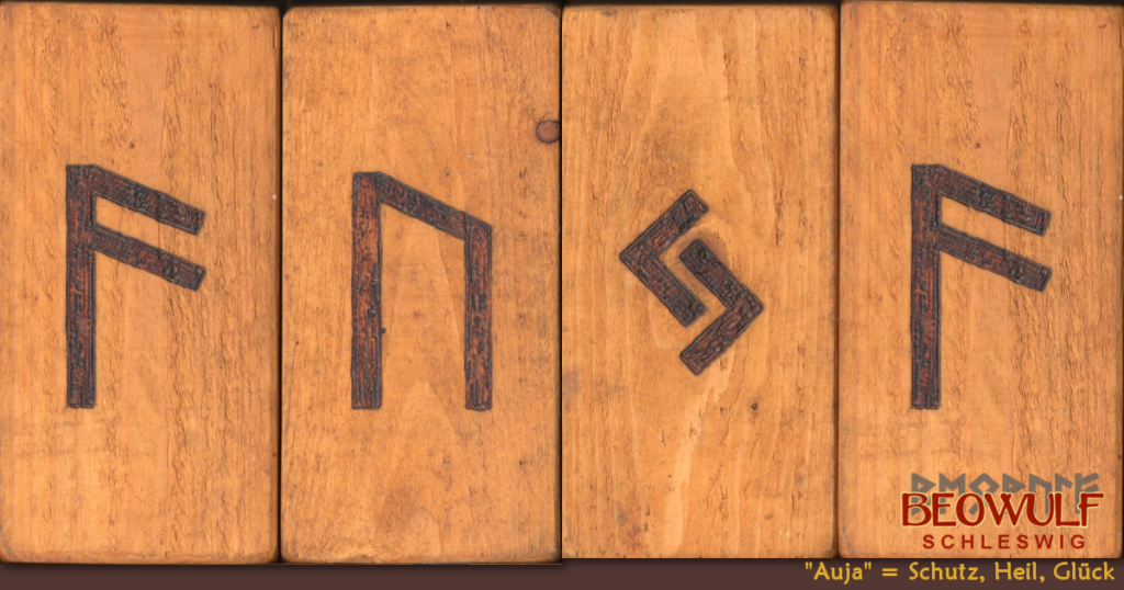 Vier nebeneinanderliegende Holztafeln, auf denen jeweils eine Rune dick und breit eingebrannt ist. Zusammen ergeben sie eine Runenformel, die mehrfach überliefert wurde: AUJA