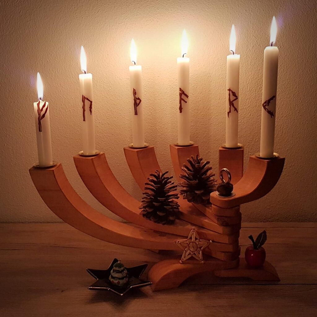 Das Bild zeigt einen winterlich dekorierten Holzleuchter, in dem sechs runenverzierte Kerzen stecken.