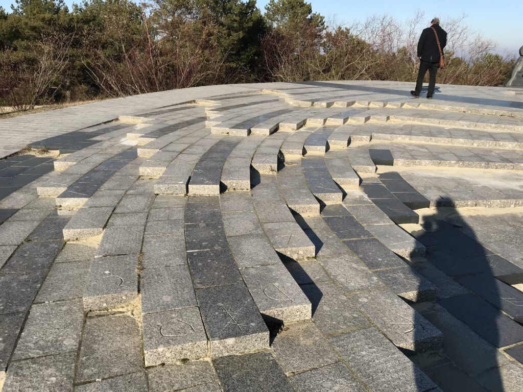 Die Grundfläche der Anlage: kreisförmig angelegte Steinringe, die gleichmäßig in kleinen Stufen enden. An jeder Stufe ist ein Zeichen, das einen Tag markieren wird, wenn der Schatten der Spitze darauf fällt.