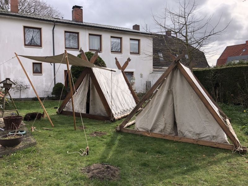 Beide Wikingerzelte aus leinenbespannten Holzlatten-Kontruktionen nebeneinander aufgebaut, vor dem einen das Sonnensegel.